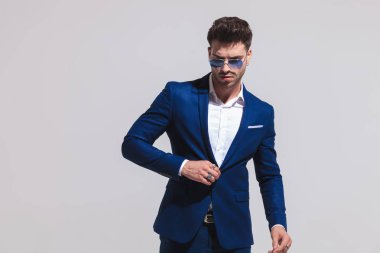 takım elbise ve Görünüm aşağı gri arka plan üzerinde poz süre kadar düğmelerini dramatik seksi adam