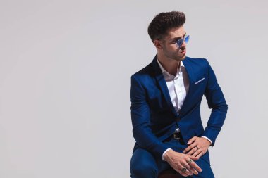 zarif delikanlı oturur ve uzak bir tarafına gri studio arka plan üzerinde görünüyor