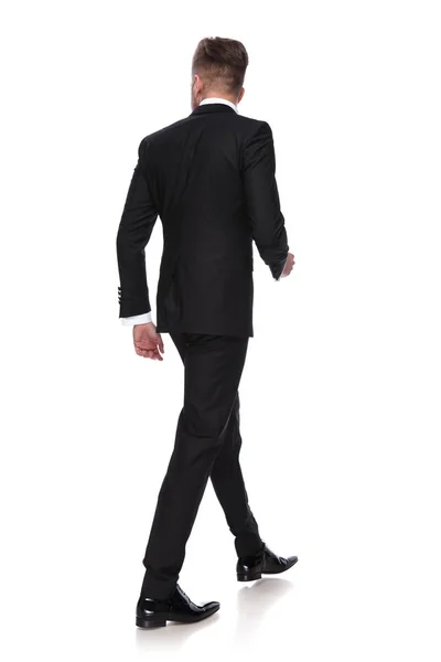 一个穿着燕尾服走路的年轻人的背视图在白色的背景 — 图库照片