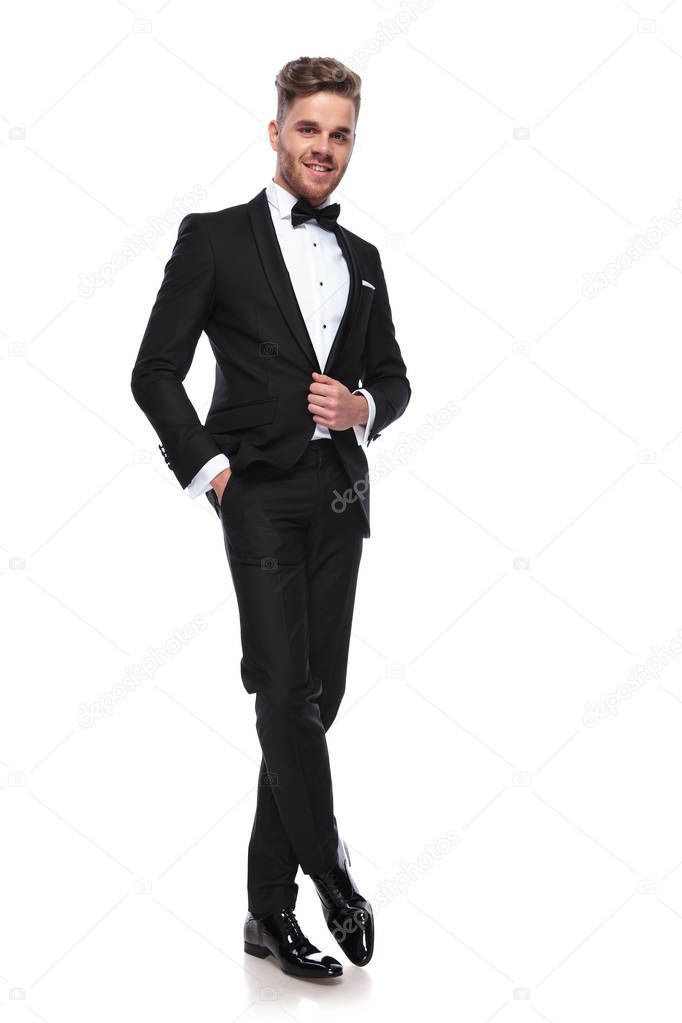happy young groom holding his coat's button while standing on white background