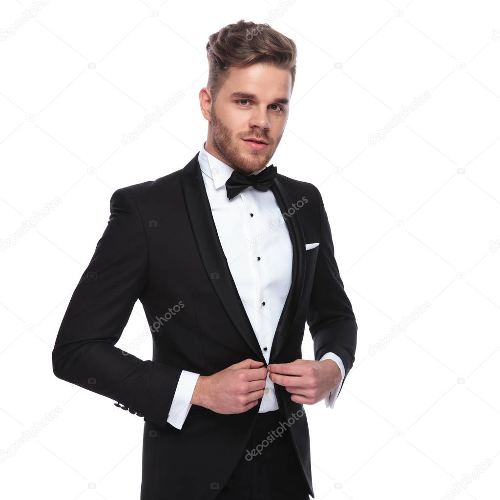 young elegant man buttoning his tuxedo on white background