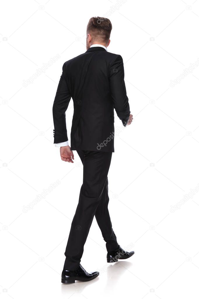 back view of a young man in tuxedo walking on white background