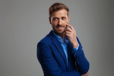 ışık gri arka plan üzerinde duran ve yanağını dokunmadan tarafına bakacak meraklı akıllı casual adam portresi