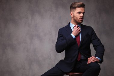 oturan işadamı tarafına gri duvar kağıdı arka plan üzerinde kırmızı papyon sabitleme ve dokunaklı onun uyluk, portre resim görünüyor