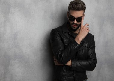 deri ceketli genç adamı dururken güneş gözlüklerini gri arka plan üzerinde portre resim giderir.