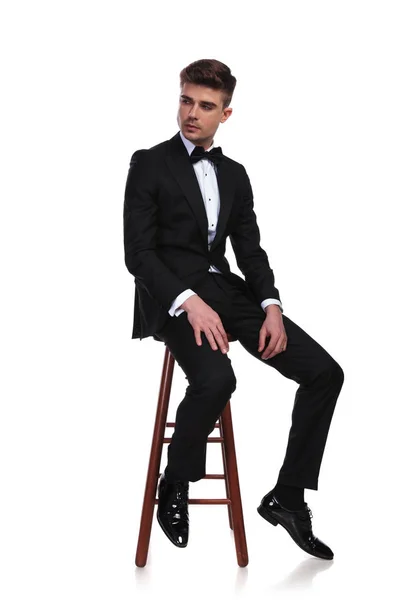 Portret Młodego Siedzącego Grooma Noszenie Czarny Smoking Patrząc Bok Białym — Zdjęcie stockowe