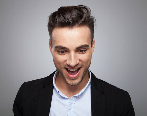 портрет удивленного случайного человека, смотрящего вниз с открытым ртом, стоя на светло-сером фоне
