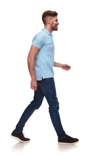白い背景と 笑みを浮かべて 完全体の画像の上を歩く青いポロシャツでカジュアルな人の側面図 — ストック写真