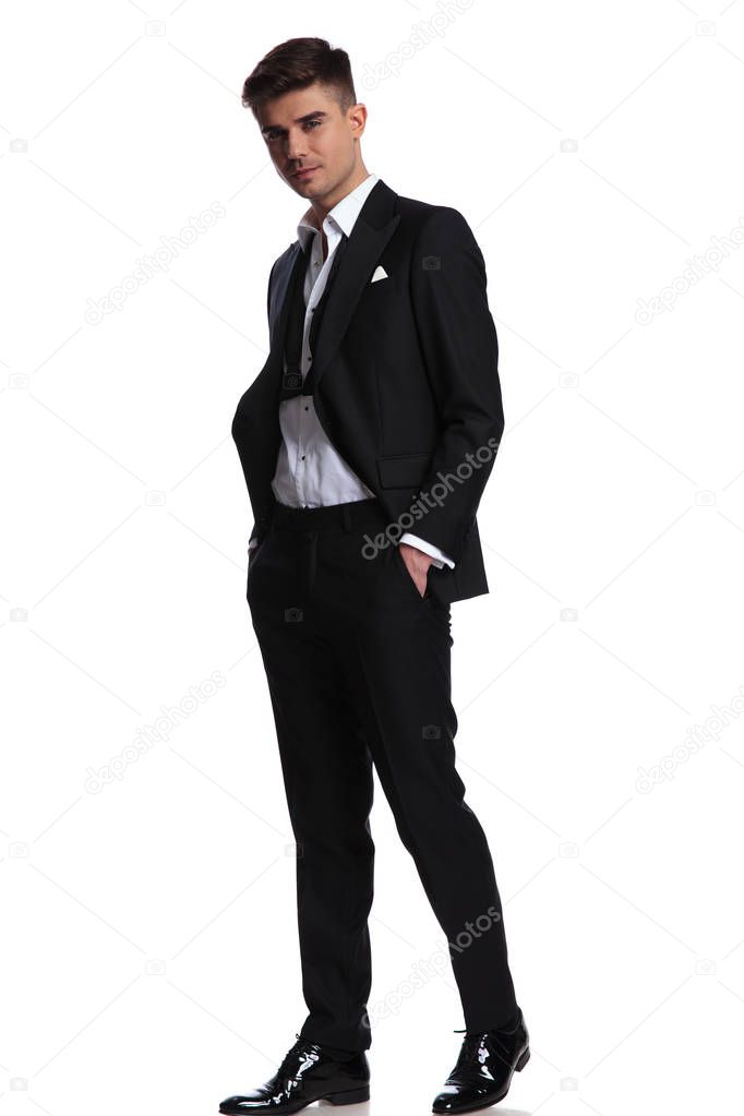 relaxed happy businessman wearing a black tuxedo walks to side on white background and smiles