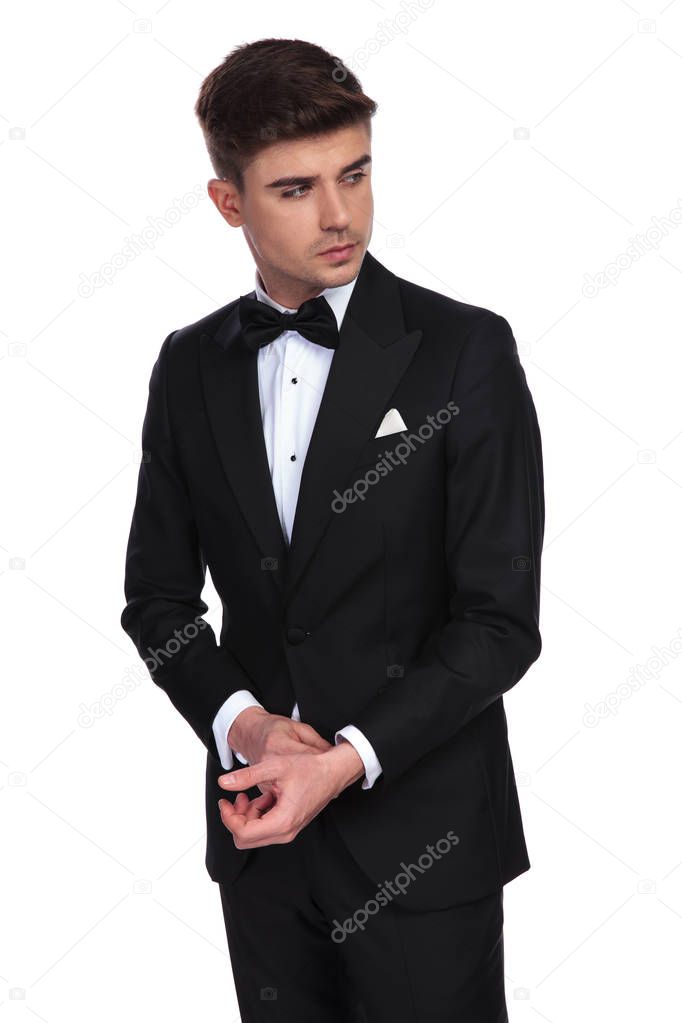 portrait of curious businessman fixing his cuffs standing on white background and looking to side