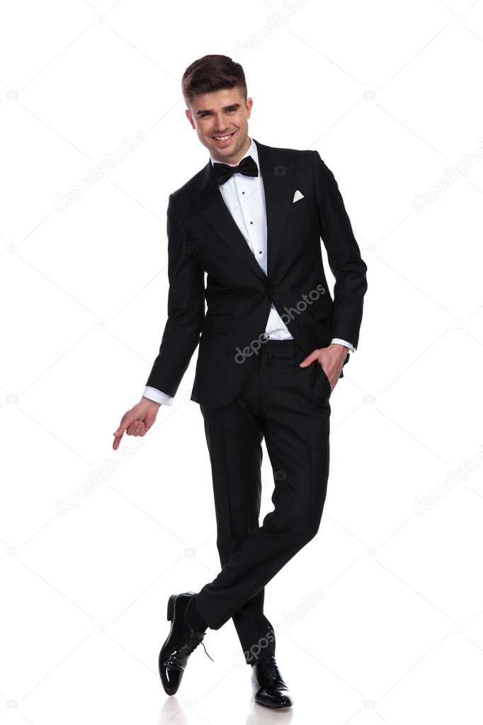 relaxed joyful businessman stands on white background cross-legged and points to side, full body picture