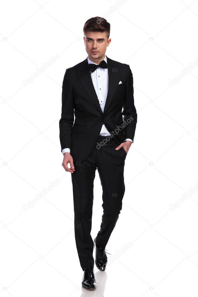 attractive relaxed groom steps forward on white background and looks to side
