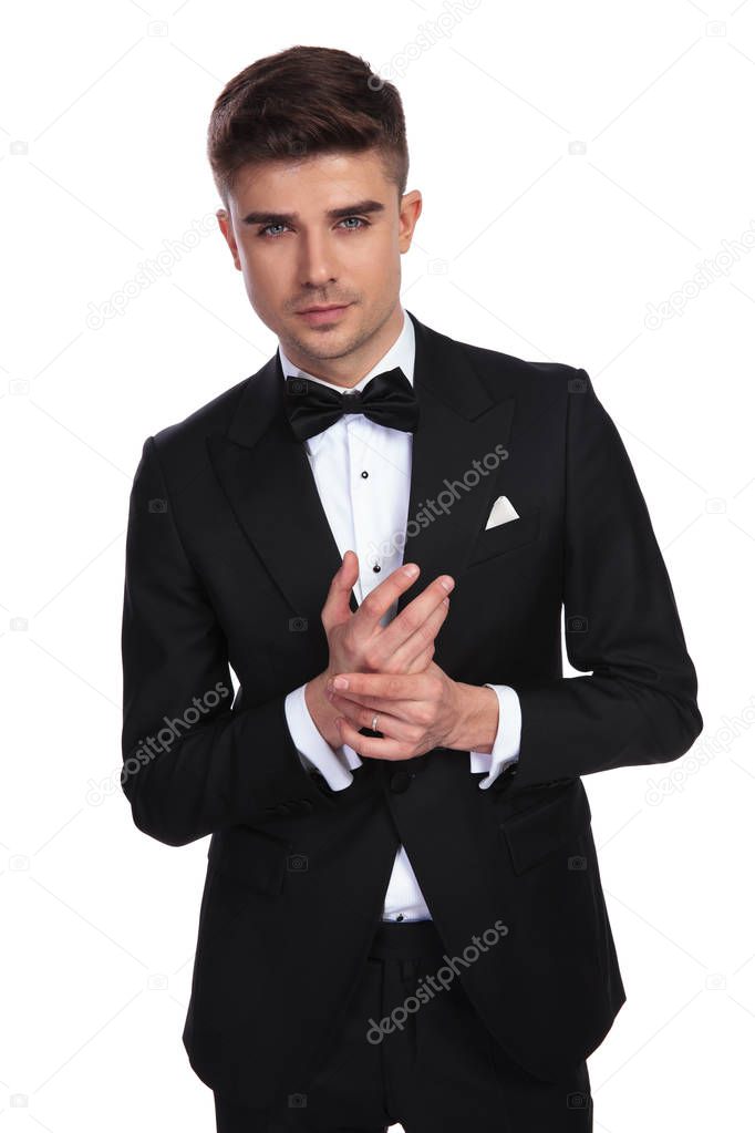 portrait of young man in black tuxedo holding palms together while standing on white background