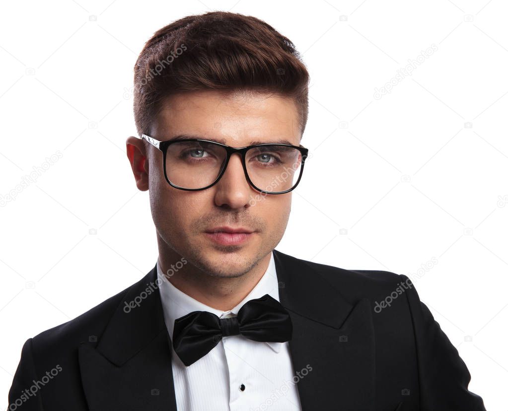 portrait of handsome smart man wearing sunglasses and black tuxedo while standing on white background