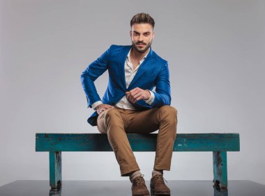 yakışıklı smart casual adam mavi ahşap bankta oturan öne eğildi hafif gri arka plan üzerinde tam vücut resim