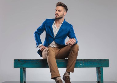 kibirli smart casual adam mavi ahşap bankta oturan tarafına, tam vücut resim görünüyor