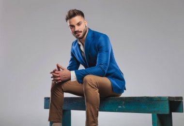 Açık gri renkli tahta bankta oturan ve avuç içi bir arada tutan mavi takım elbise genç adam portresi