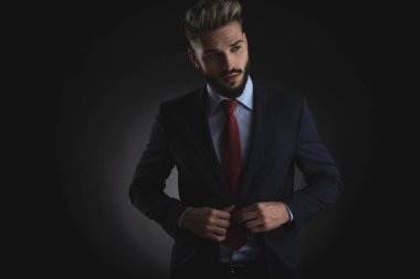 takım elbise kadar düğmelerini ve siyah arka plan üzerinde dururken ayrık dudaklı tarafına bakarak genç çekici işadamı portresi