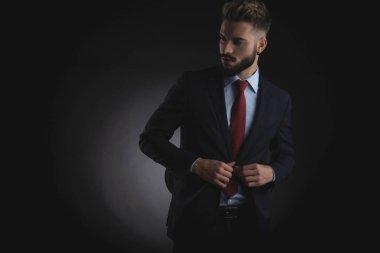 meraklı işadamı unbuttoning takım elbise ve siyah arka plan üzerinde dururken tarafa bakıyor portre