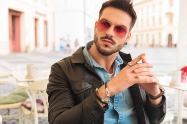 Şehir merkezinde masada otururken tarafına bakan güneş gözlüğü takıyor ve avuç içi bir arada tutan moda adam