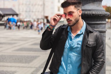 bir eli cebinde olan şehirde ayakta ve aydınlatma direği karşı yaslanmış iken kırmızı güneş gözlüğü sabitleme meraklı casual adam portresi