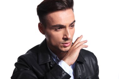 Beyaz arka plan üzerinde duran ve çene tutan tarafına deri ceketli meraklı işadamı görünüyor