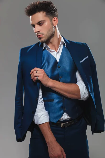 上品な男性のスーツの襟を押しながら側を見下ろすと ライトグレーの背景の上に立っての肖像画 — ストック写真