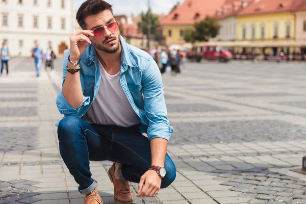 Curious Casual Man Crouching City Fixes Red Sunglasses While Looking — Stock Photo, Image