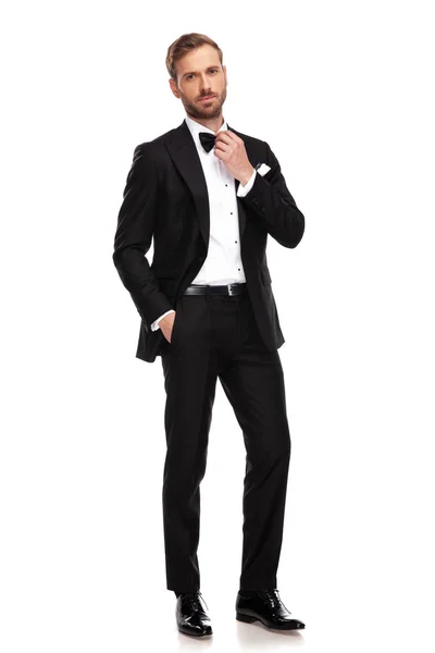 黒のスーツが白い背景のフルの長さの画像上に立っている間彼のボウタイを固定でリラックスした実業家 — ストック写真