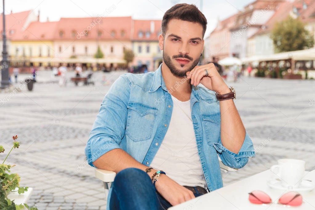 portrait of seated young casual man on urban background wearing rings and bracelets