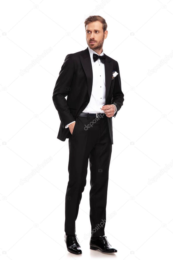 relaxed businessman holds pocket and looks to side while standing on white background, full length picture