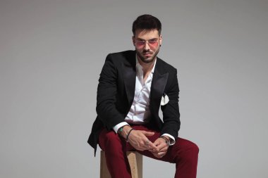 Ahşap sandık üzerinde oturan ve birlikte elele kırmızı güneş gözlüğü takıyor akıllı casual adam portresi