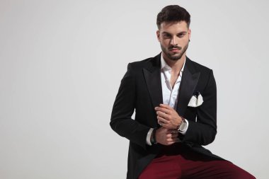 kırmızı pantolon ve açık gri renkli saatini tamir siyah takım elbise giyen oturan zarif adam portresi