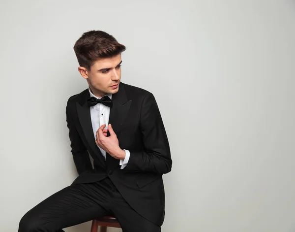 Curious Groom Holding Tuxedo Collar Looks Side While Sitting Wooden — Stock Photo, Image