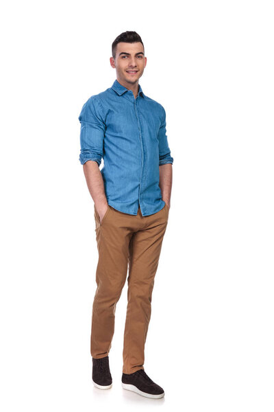 happy casual man wearing blue shirt standing on white background with hands in pockets, full length picture