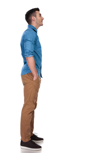 side view of relaxed casual man looking up at something while standing on white background