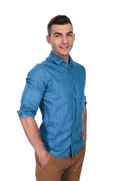 portrait of relaxed handsome man wearing blue shirt standing on white background with hands in pockets