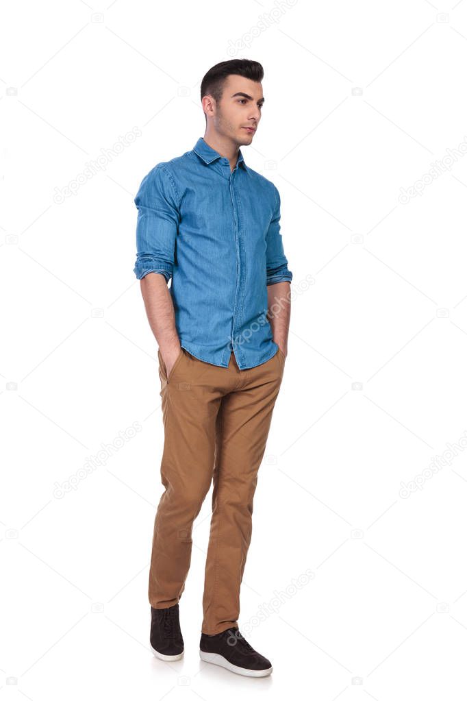 handsome casual man walks to side with hands in pockets on white background