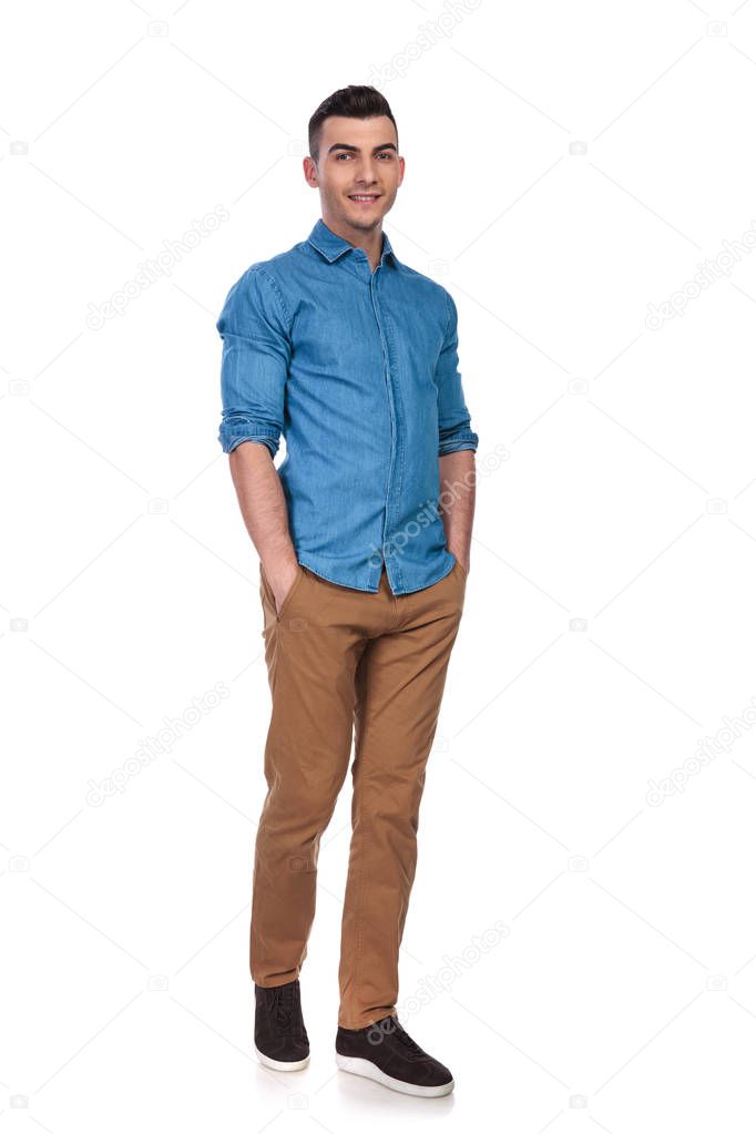 happy casual man wearing blue shirt standing on white background with hands in pockets, full length picture