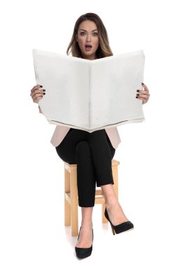 shocked businesswoman sits on wooden stool while holding newspaper on white background, full length picture clipart