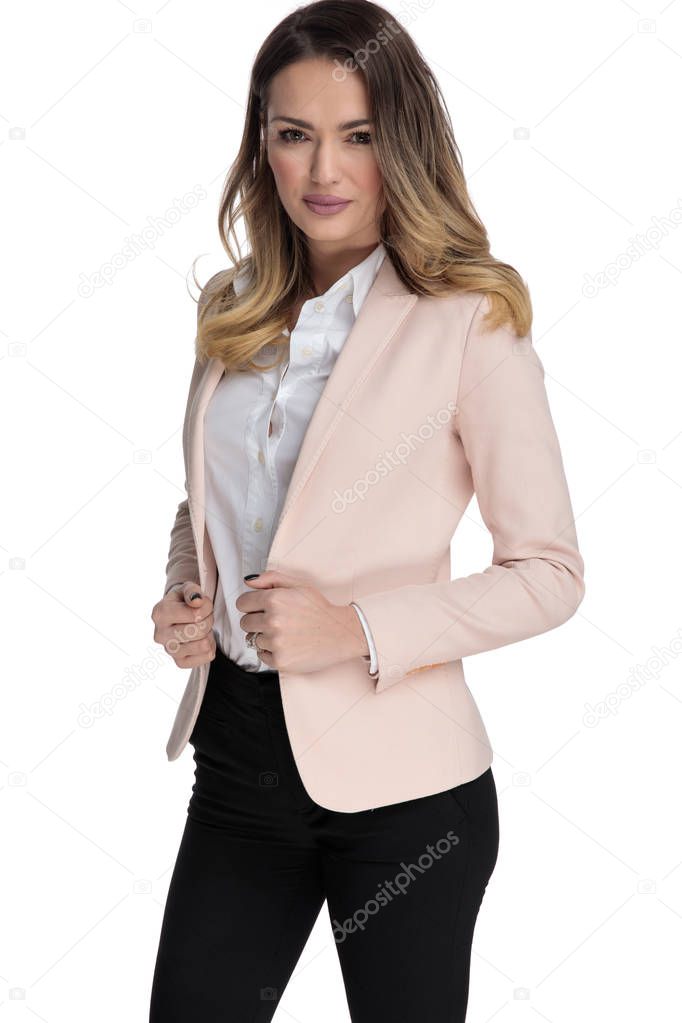 portrait of sexy businesswoman holding pink suit collar while standing on white background