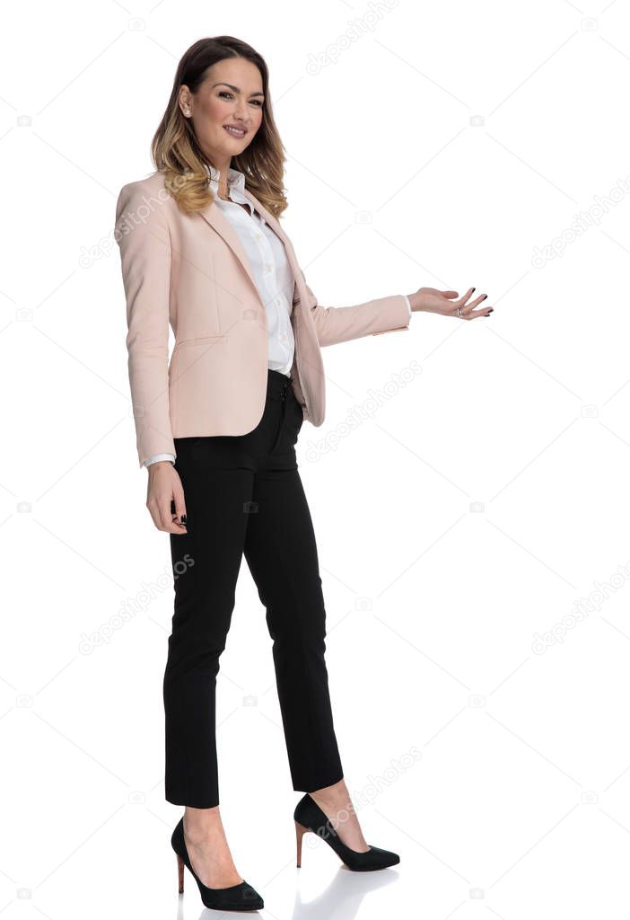 young businesswoman in high heels presents to side while standing on white background, full length picture