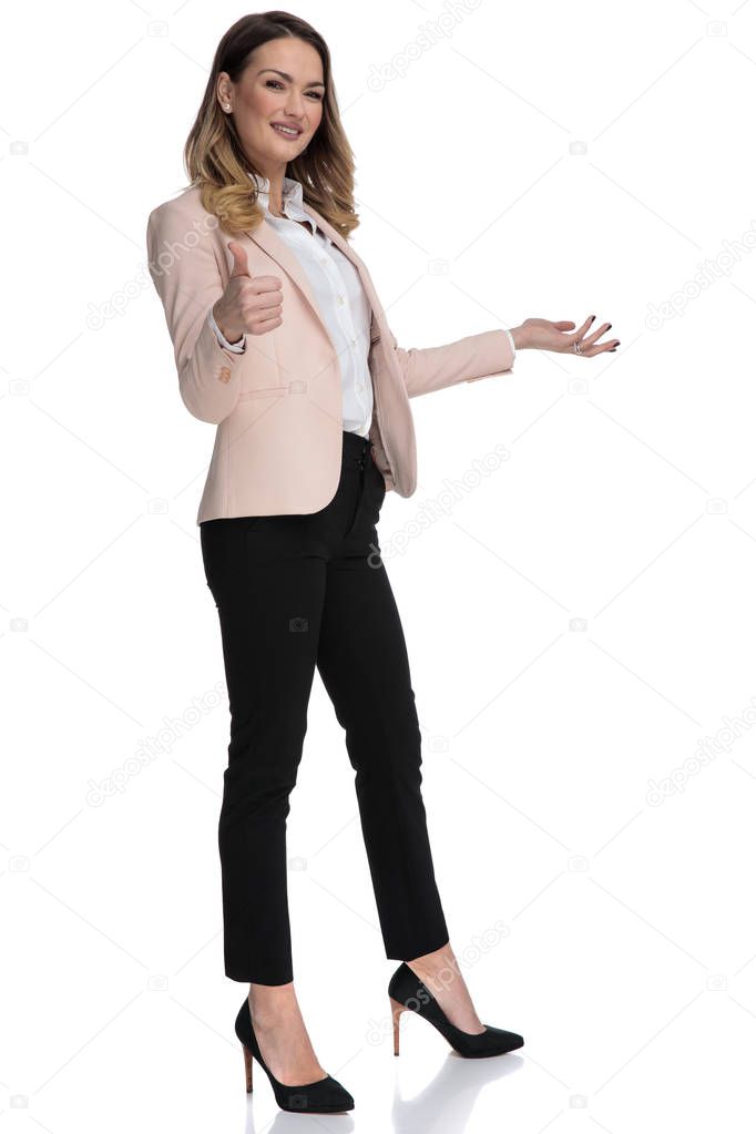 attractive businesswoman makes thumbs up sign and presents to side while standing on white background, full body picture