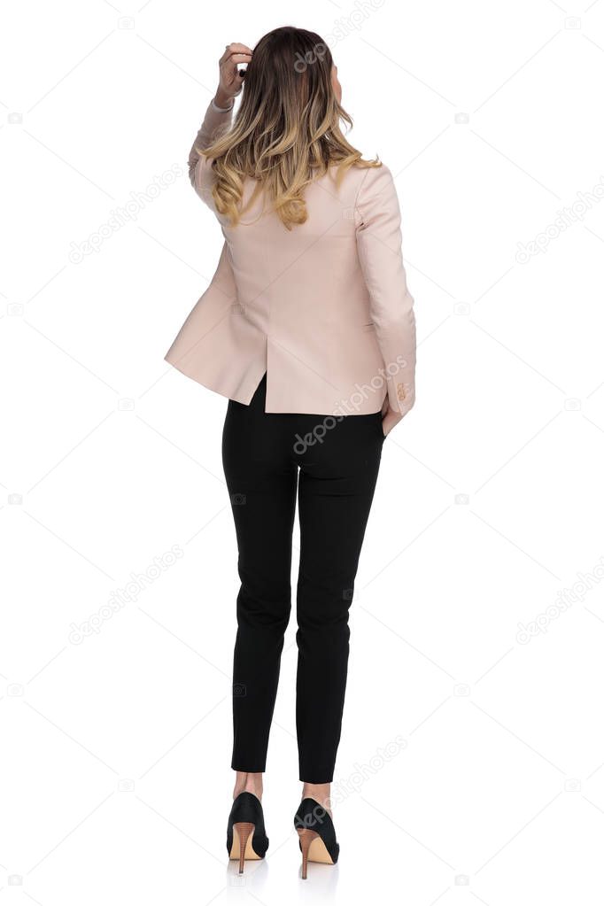 back view of pensive businesswoman looking up to side while standing on white background, full length picture