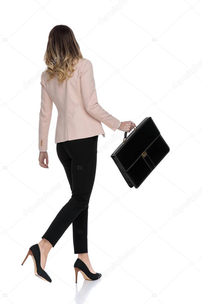 rear view of attractive businesswoman walking to side on white background and holding suitcase, full length picture