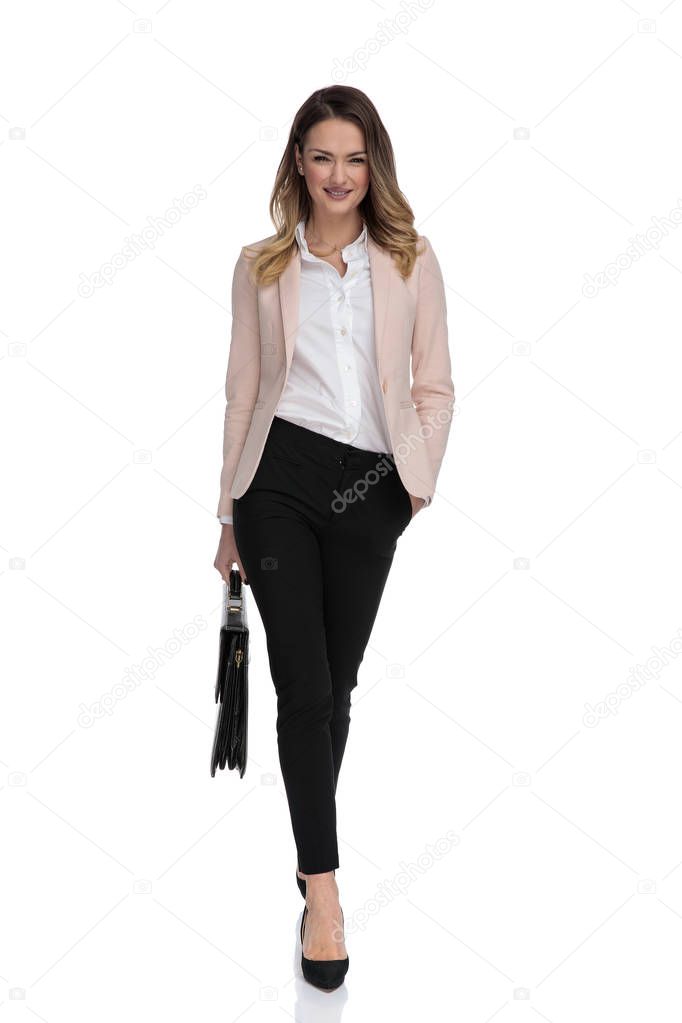relaxed businesswoman with black suitcase walks to work on white background with hand in pocket, full body picture