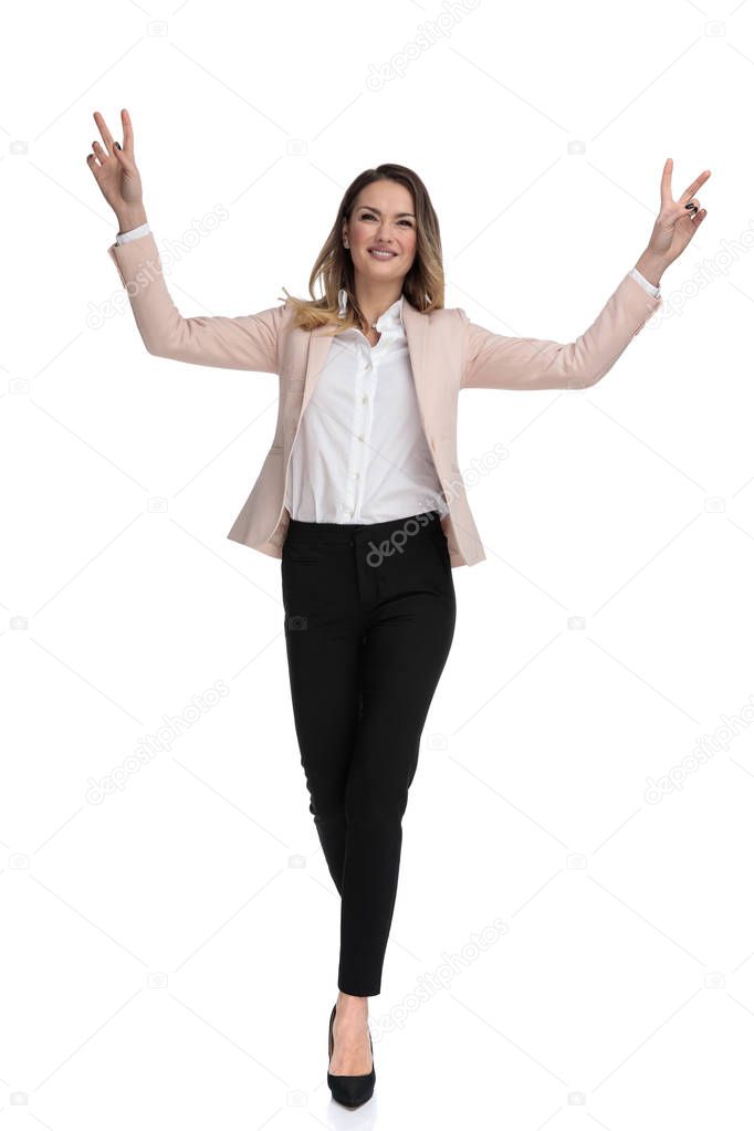young smart casual woman celebrates and makes peace sign while stepping forward on white background, full body picture