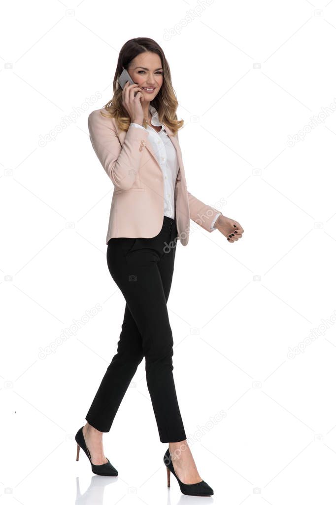 attractive businesswoman speaking on the phone moves to side on white background and smiles, full body picture