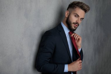 yan görünüm portre gülümseyen genç işadamı kravatını ayarlama ve kameraya gri arka plan üzerinde seyir