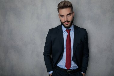 Elleri ceplerinde gri studio wal karşı ayakta rahat genç moda işadamı
